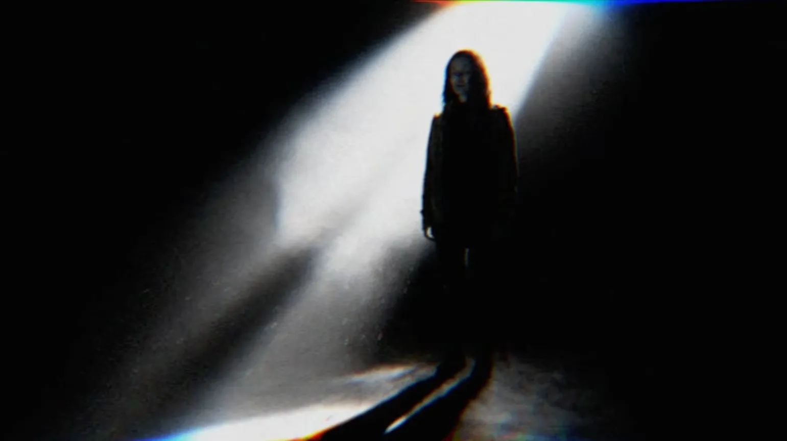 A figure in a beam of light in a dark room